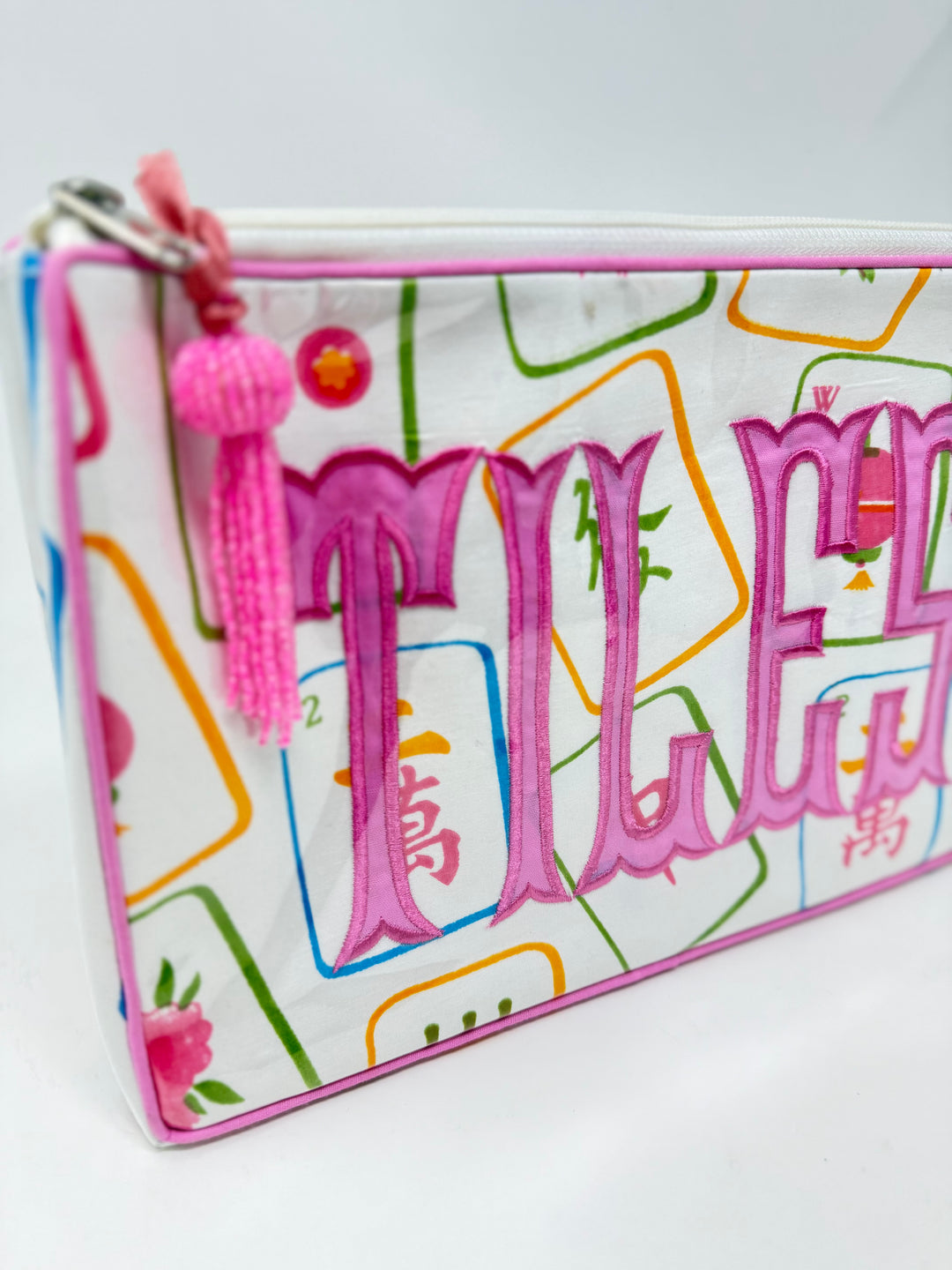 Tiana Design Mahjong Cosmetic Bag with pink embroidered 'TILES' text and a pink tassel zipper pull.