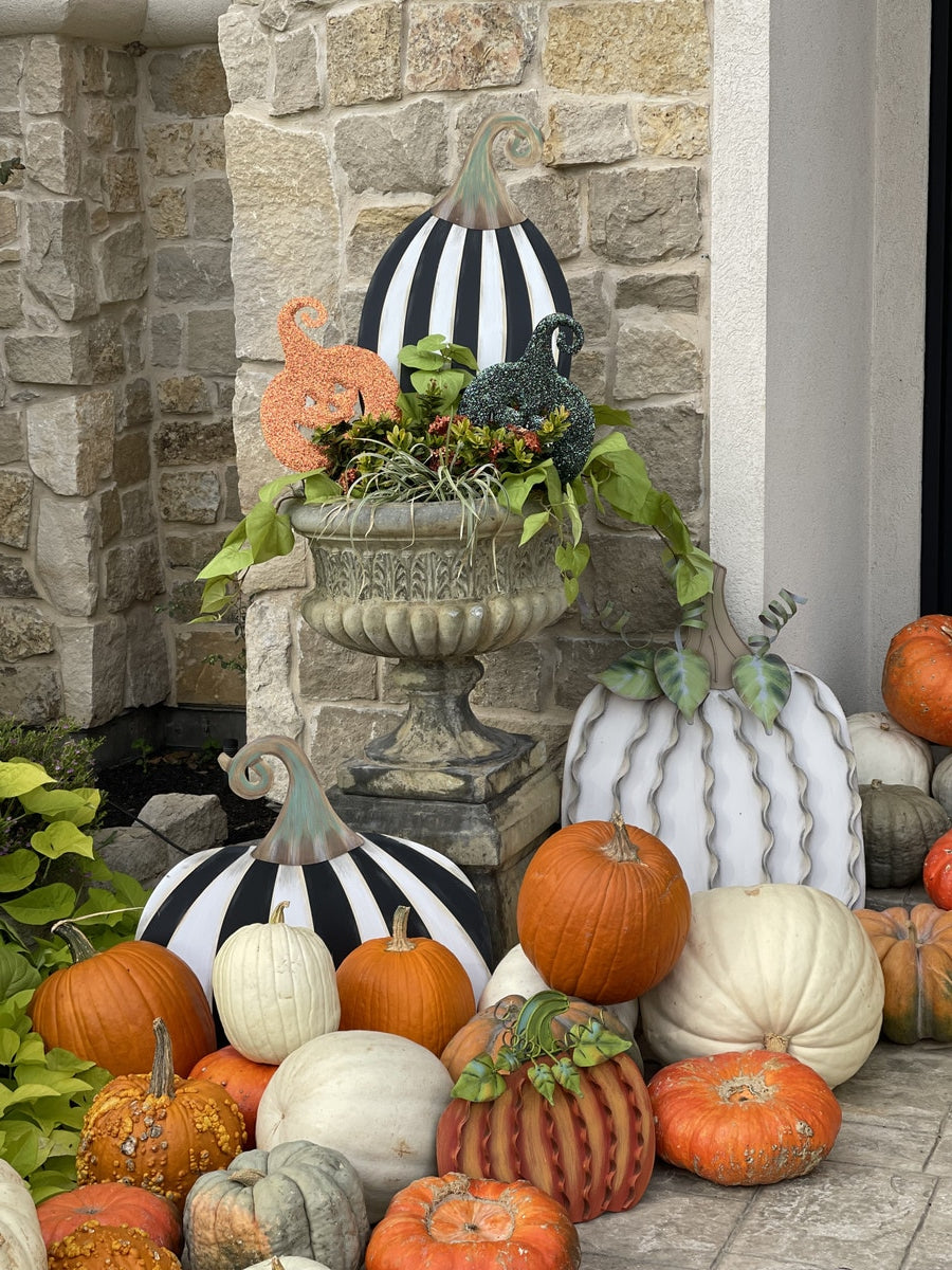 Short black and white striped pumpkin yard art with a curved stem displayed among real pumpkins.