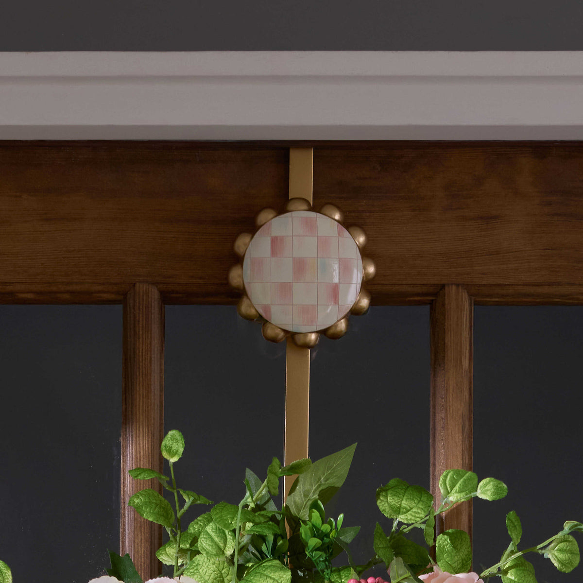 Resin wreath hanger with rosy checkered metal accents in a curved silhouette.