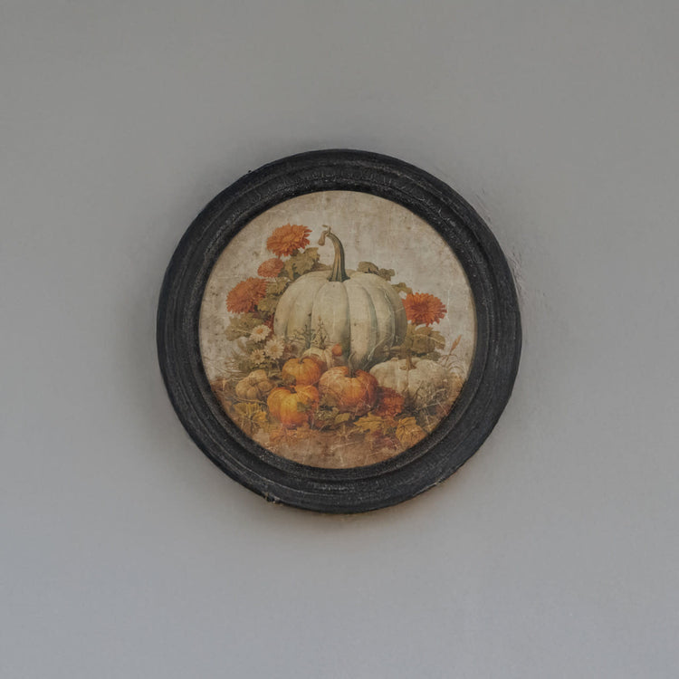 Round framed print showing a pumpkin patch scene with autumn colors on glass over wood.