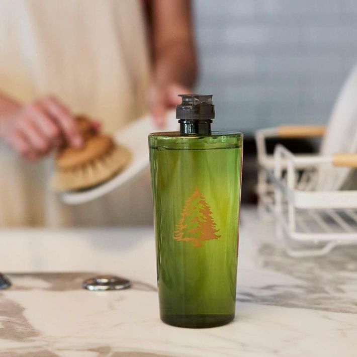 Frasier Fir Dishwashing Liquid in a green bottle with a gold tree logo on a kitchen counter.