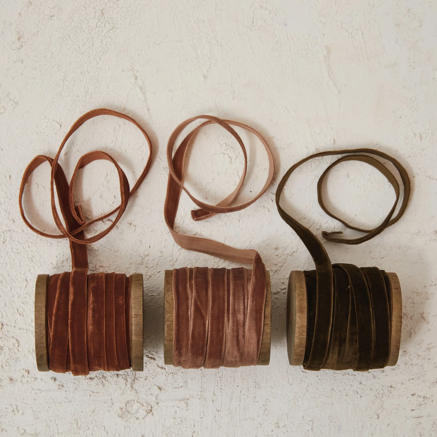 Three wooden spools of 1/4 inch velvet ribbon in rust, dusty rose, and olive green colors.