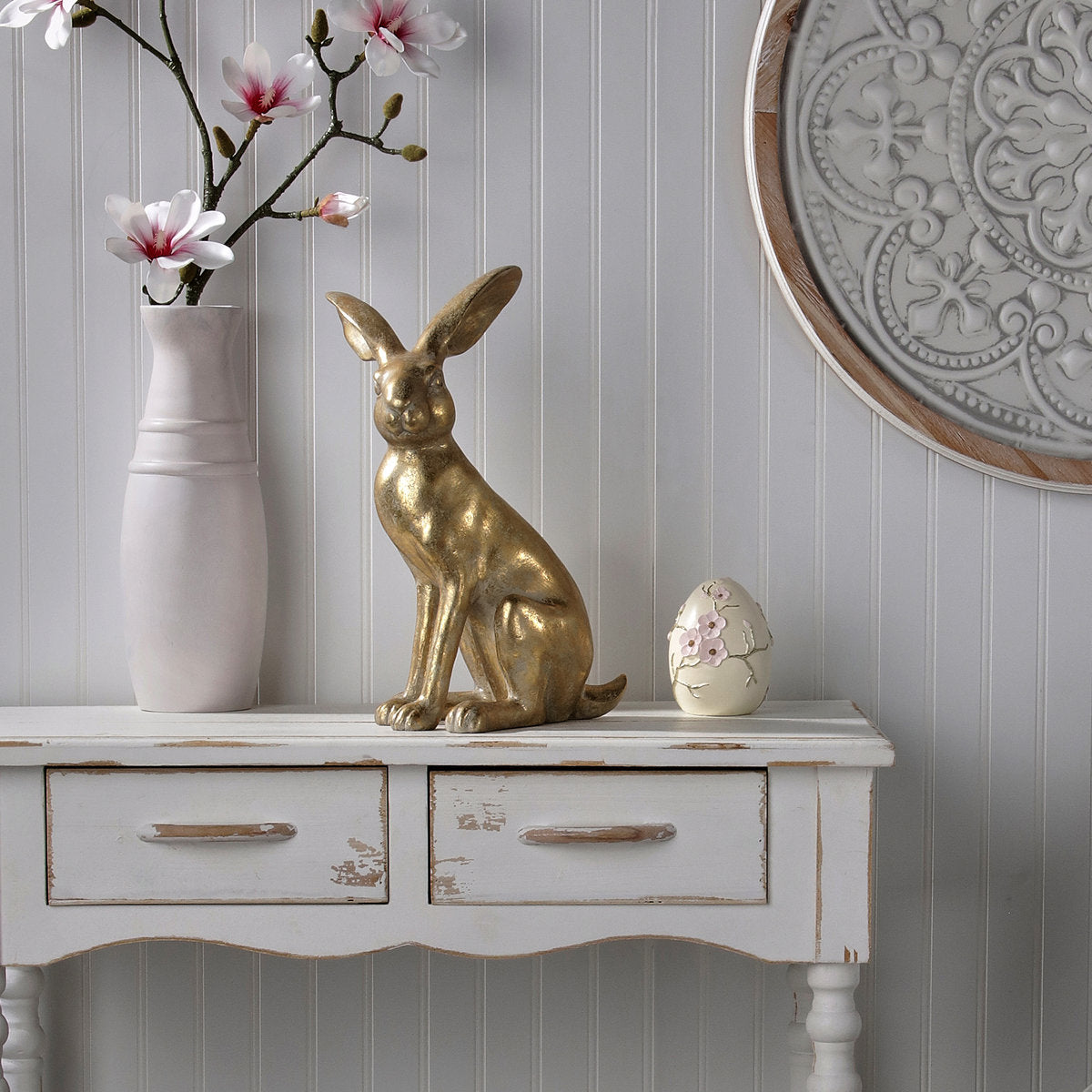 15.5-inch golden resin bunny figurine sitting on a white rustic console table.