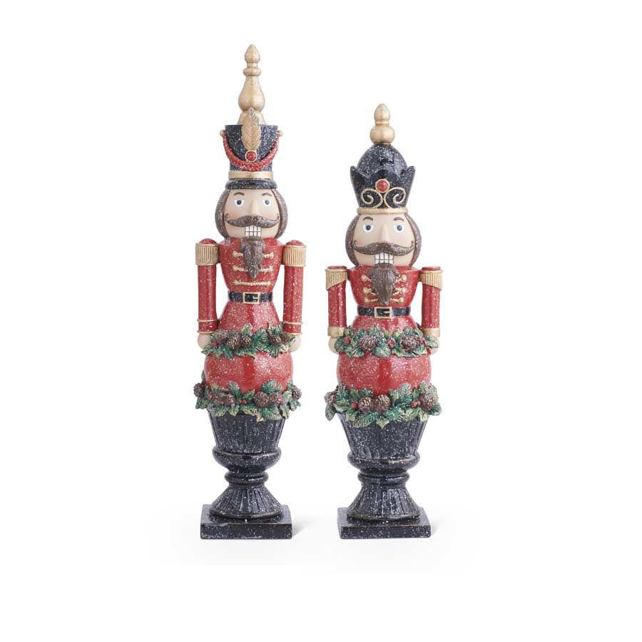 Two resin glittered nutcrackers on black pedestals with pinecone and greenery accents.
