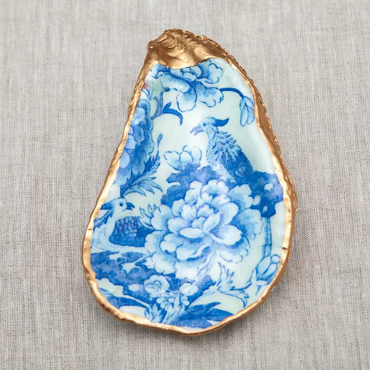 Decoupaged oyster shell with blue floral and bird pattern and metallic gold trim.