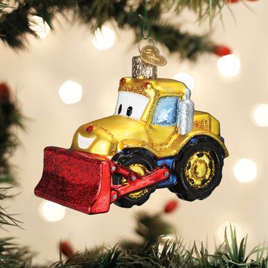 Bright Eyed Bulldozer glass ornament with a yellow body, red blade, and smiling face on a tree.