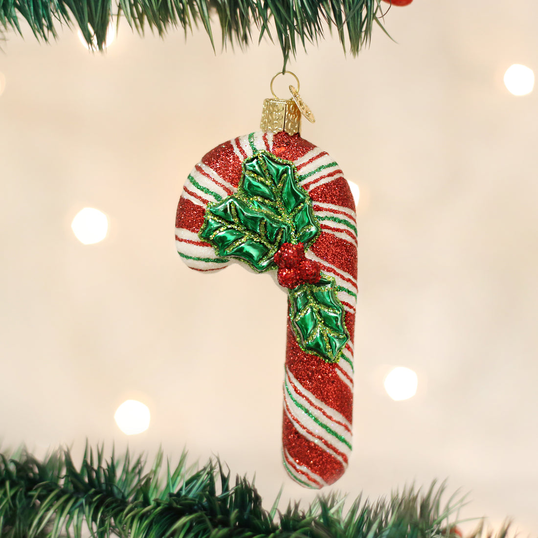 Glistening candy cane ornament with red and white glitter stripes and green holly leaf detail.