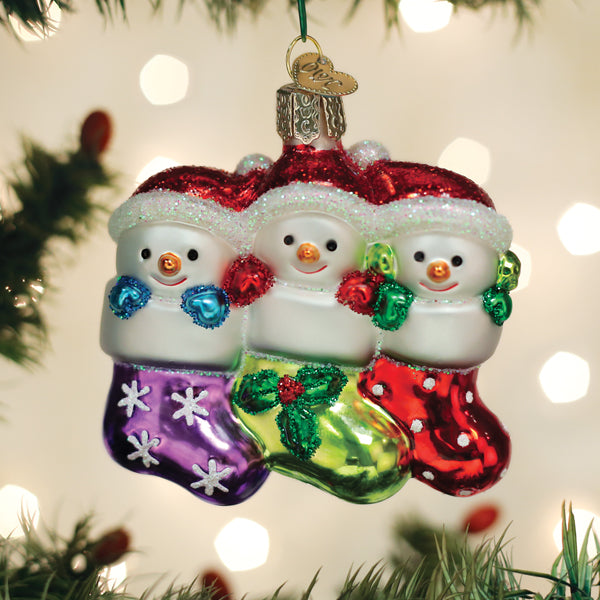 Glass ornament featuring three snowmen in purple, green, and red glittery stockings.
