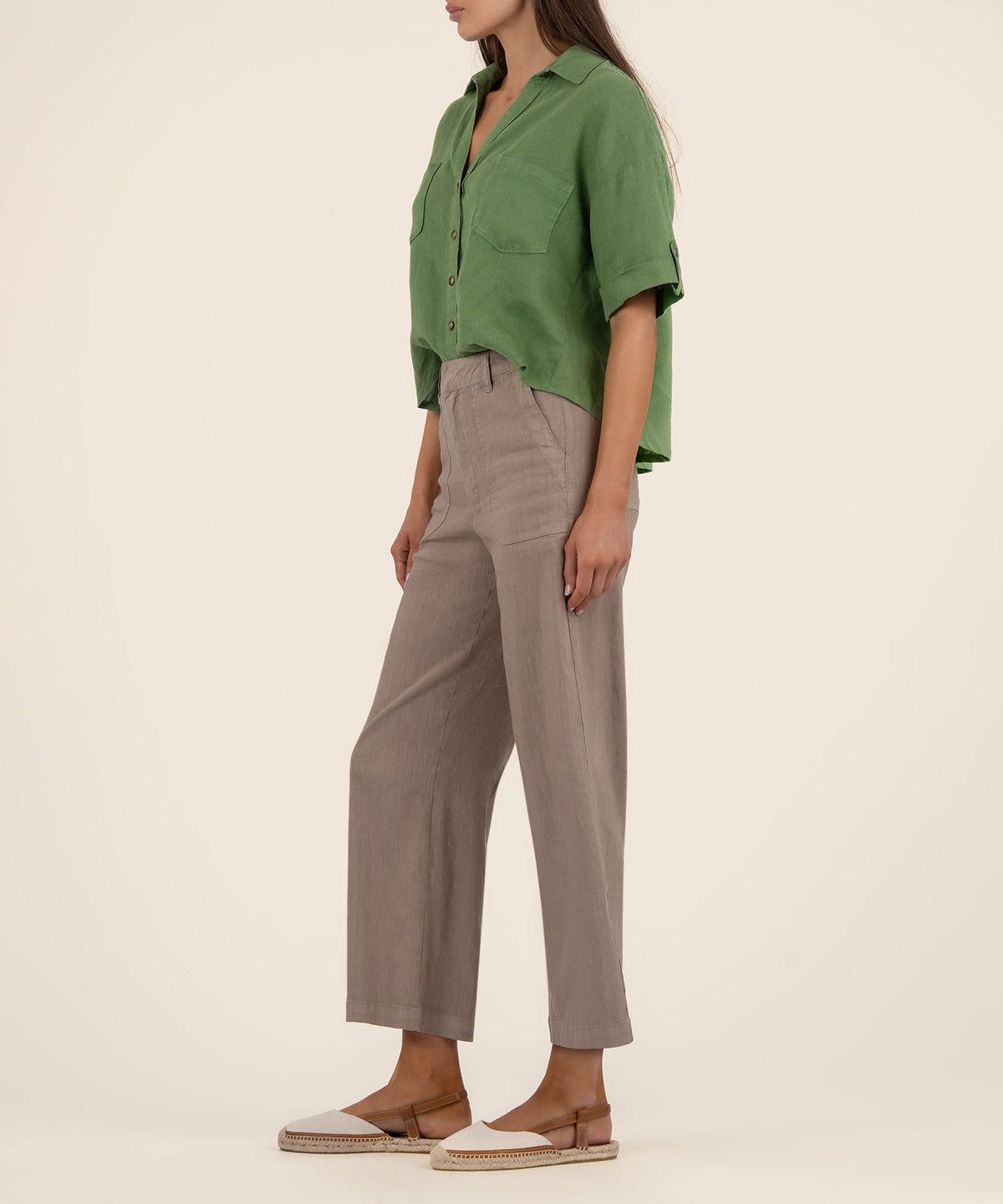 Woman wearing a green boxy short-sleeve button-front shirt with a chest pocket and taupe pants.