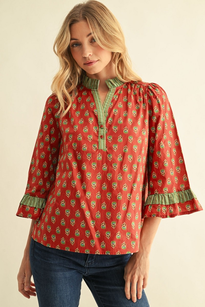 Woman wearing a red floral cotton top with 3/4 bell sleeves, green striped ruffles, and V-neckline.