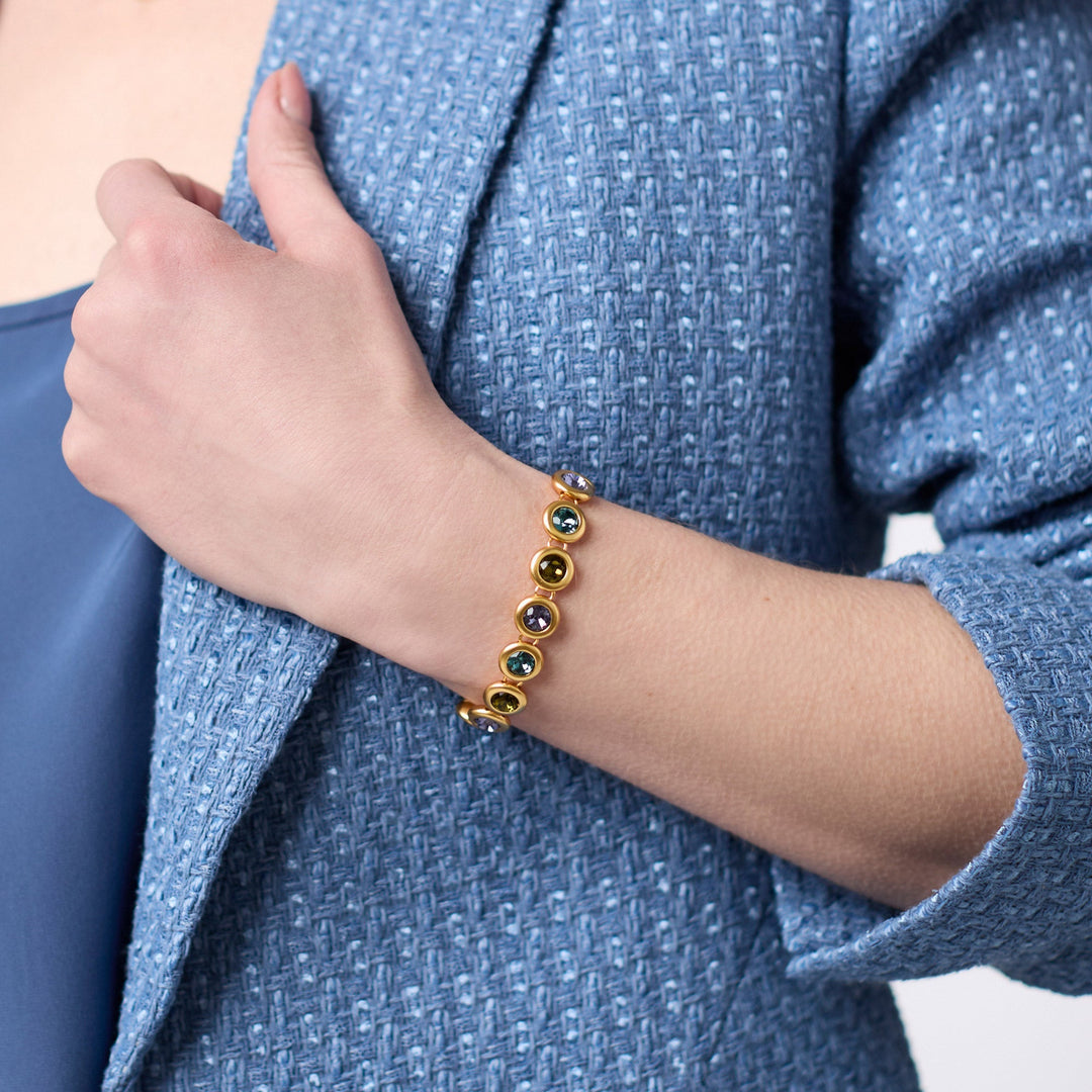 A person wearing a gold-plated Rainbow Tennis Bracelet with colorful glass stones and a blue jacket.