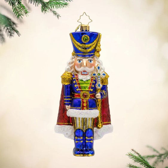 Long Coat Nutcracker glass ornament with a blue uniform, red cape, and gold glitter accents.
