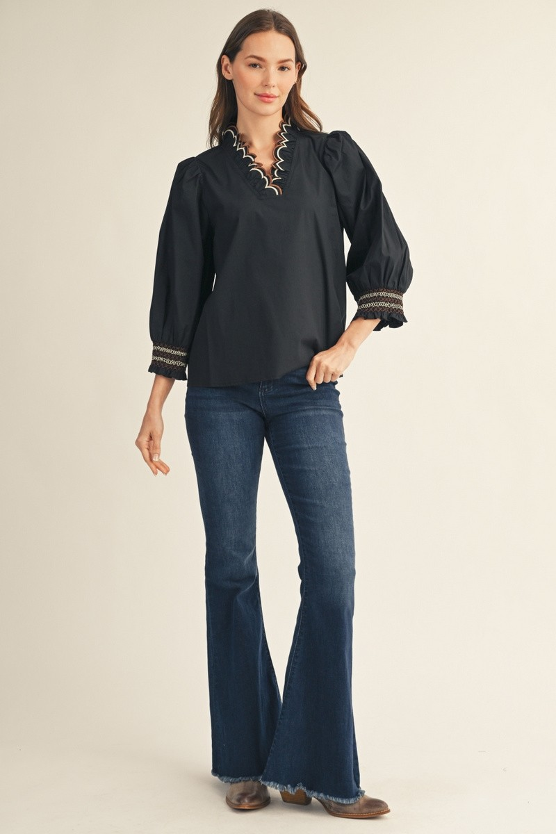 Woman in a black Millie top with embroidered scallop V-neckline and flared blue jeans.