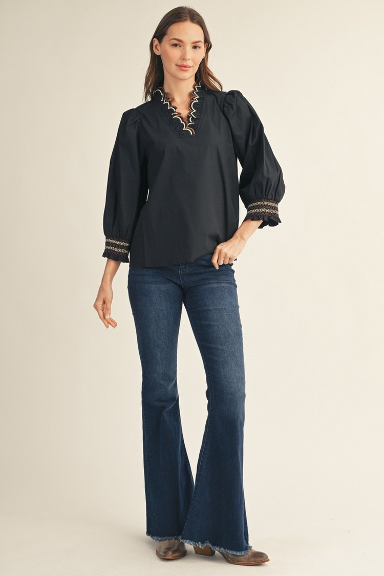 Woman in a black Millie top with embroidered scallop V-neckline and flared blue jeans.
