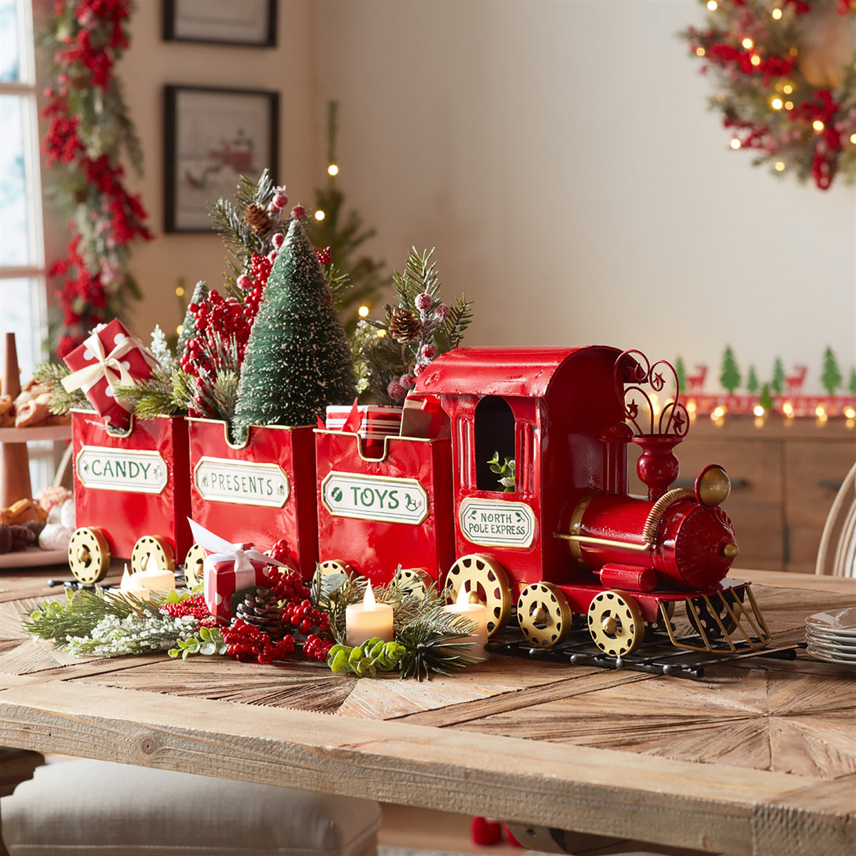 Red metal Christmas train decoration with three cars labeled Candy, Presents, and Toys, on a wooden table.