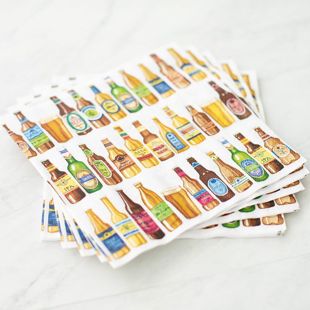Stack of white cocktail napkins featuring a colorful watercolor pattern of various beer bottles.