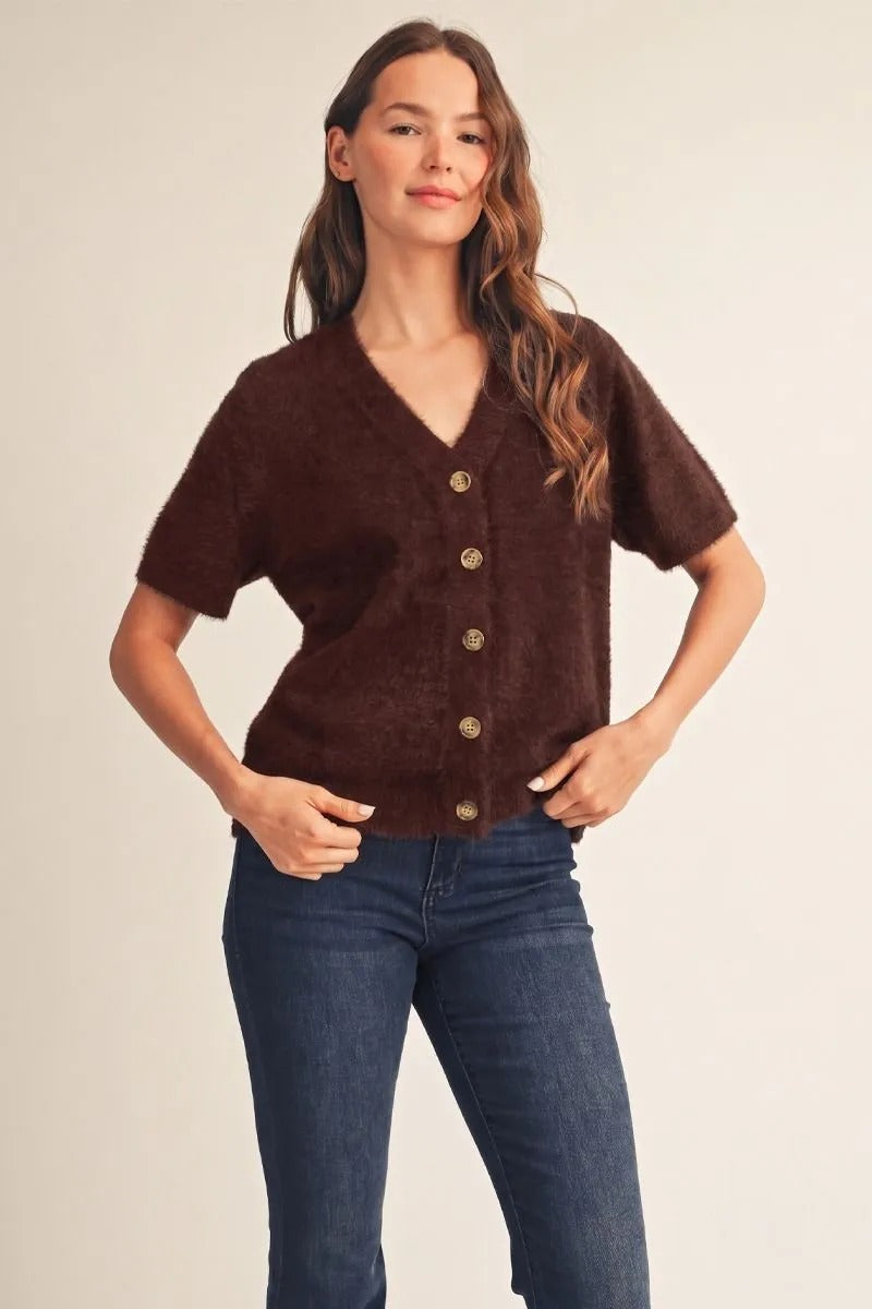 Woman wearing a brown Aurora short sleeve fuzzy button-down cardigan with dark blue jeans.