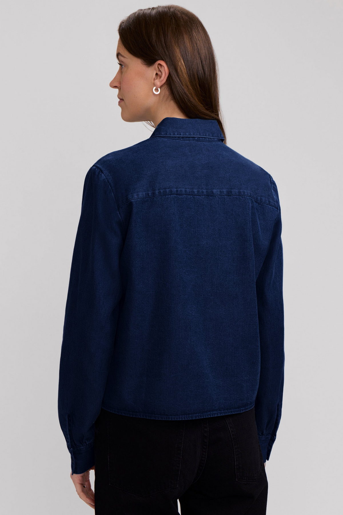 Back view of a woman wearing the Jodie Denim Long Sleeve Short Shirt in a dark blue wash.