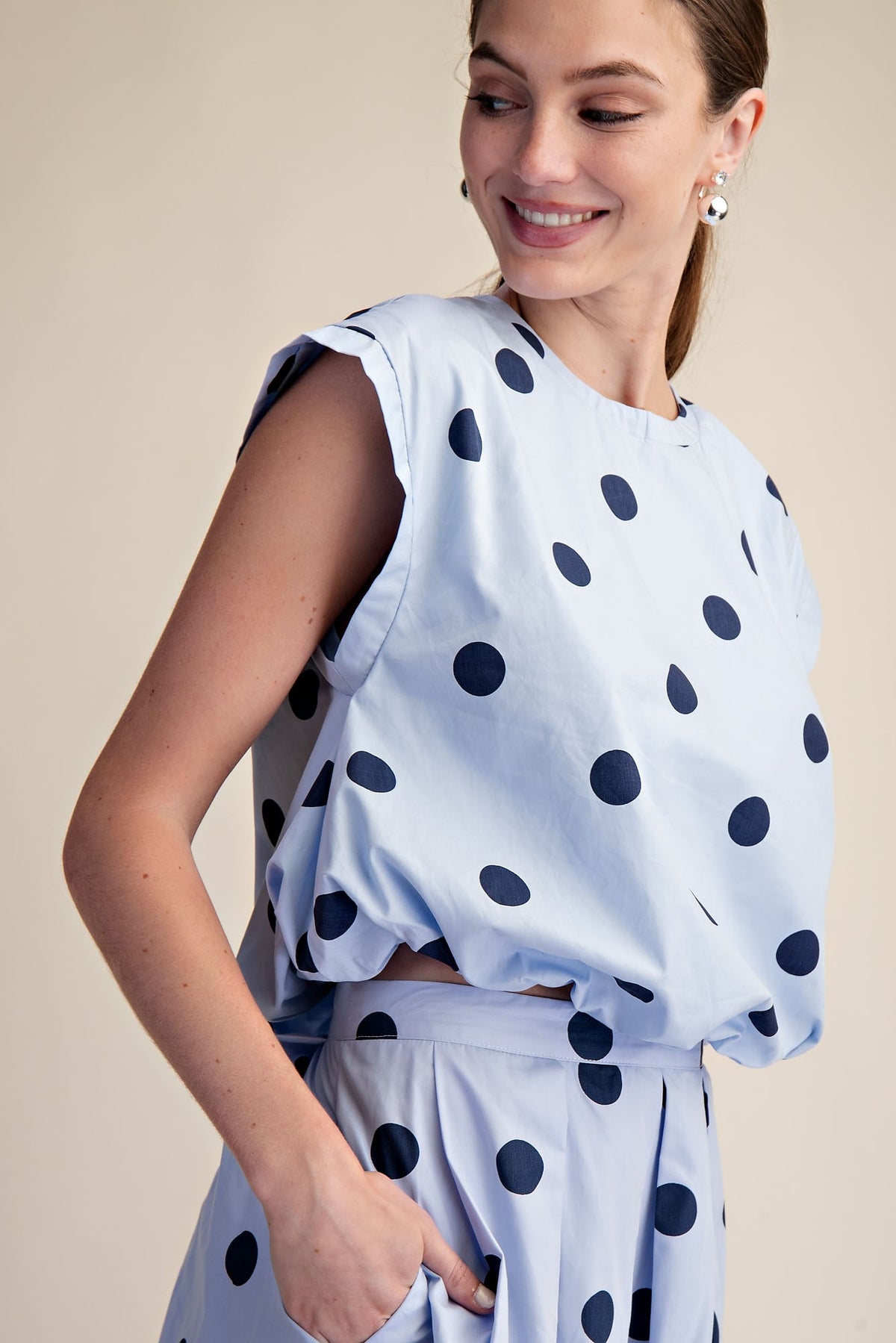 Woman wearing a light blue bubble crop top with large navy polka dots and matching skirt.