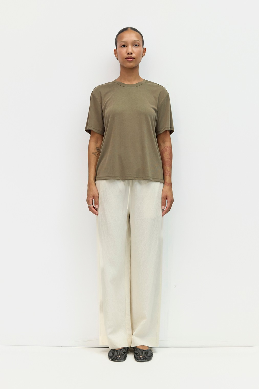 A person wearing cream-colored wide-leg Jodi pants with a drawstring waist and an olive green t-shirt.