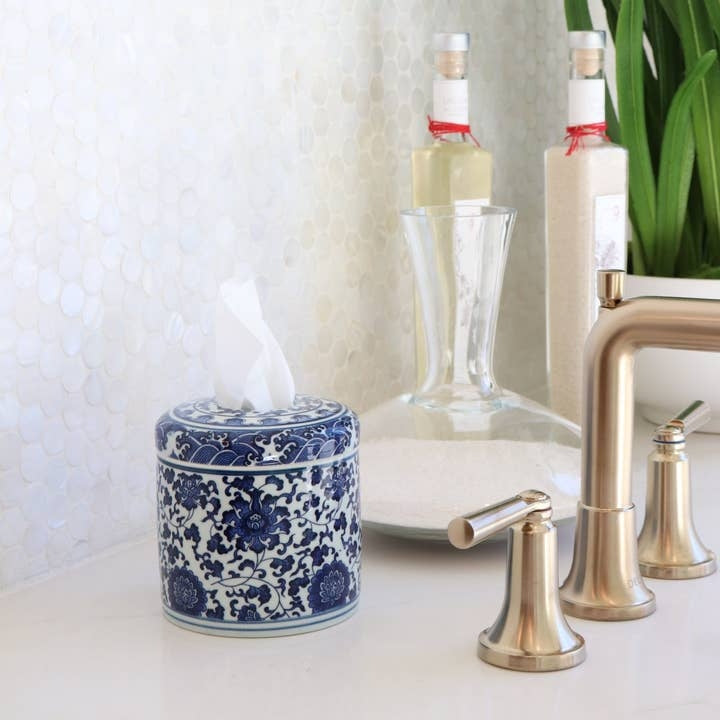 Blue and white floral ceramic tissue vessel on a white bathroom counter next to a gold faucet.
