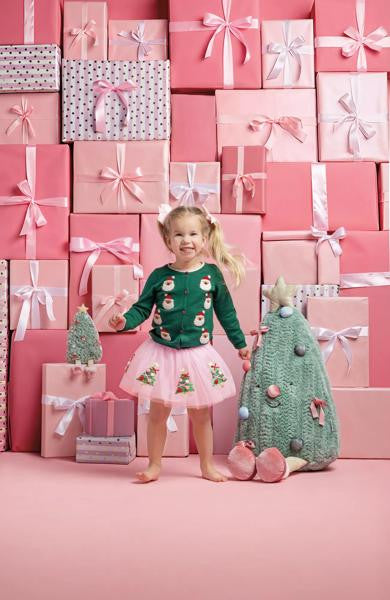 Girl wearing a pink sequin Christmas tree tutu with a green Santa cardigan in front of pink gifts.