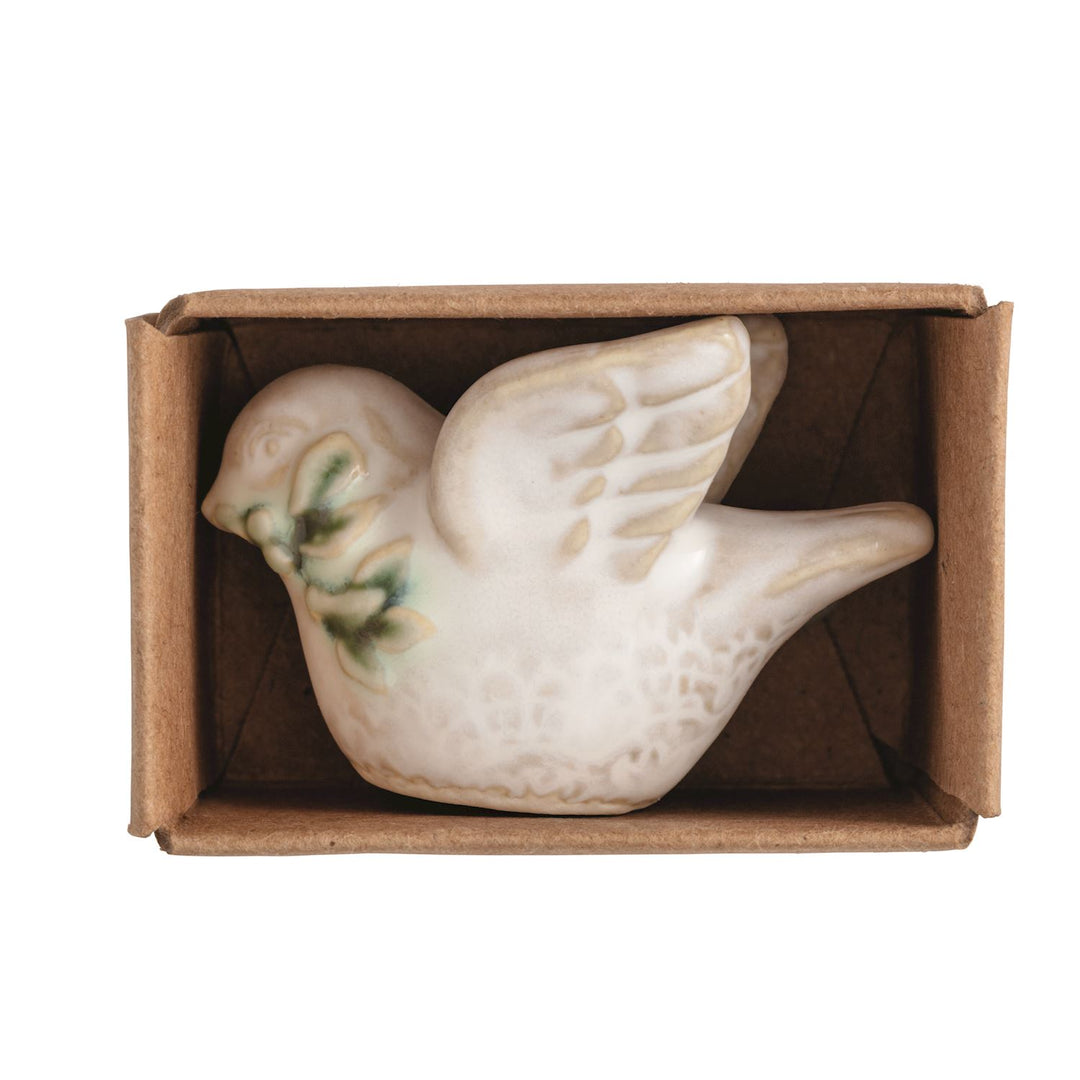A small ceramic turtledove figurine with green leaf details inside a brown cardboard gift box.
