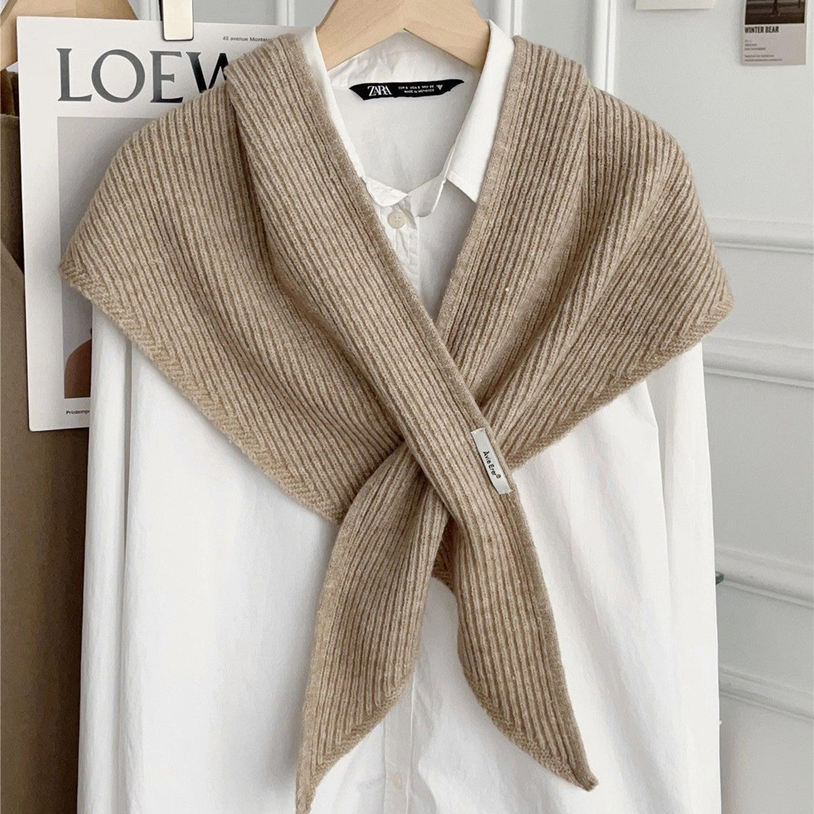 Beige knitted solid cross triangle shawl draped over a white button-down shirt on a hanger.