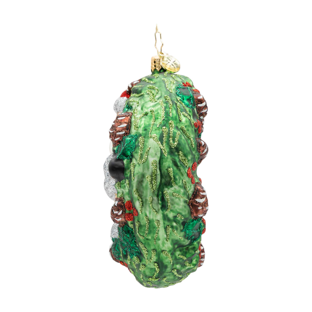 Side view of a green glass wreath ornament with glittery pine needles, holly, and red berries.
