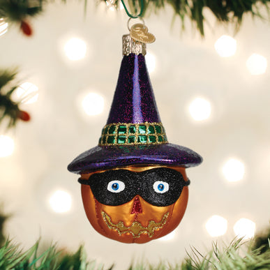 Glass pumpkin ornament wearing a black mask and a purple glittery witch hat with a green band.