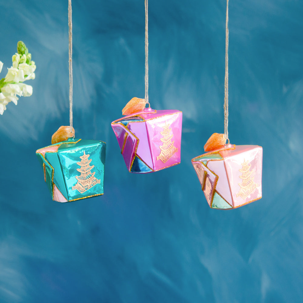 Three colorful hand-blown glass take out box ornaments in teal, purple, and pink with glitter.