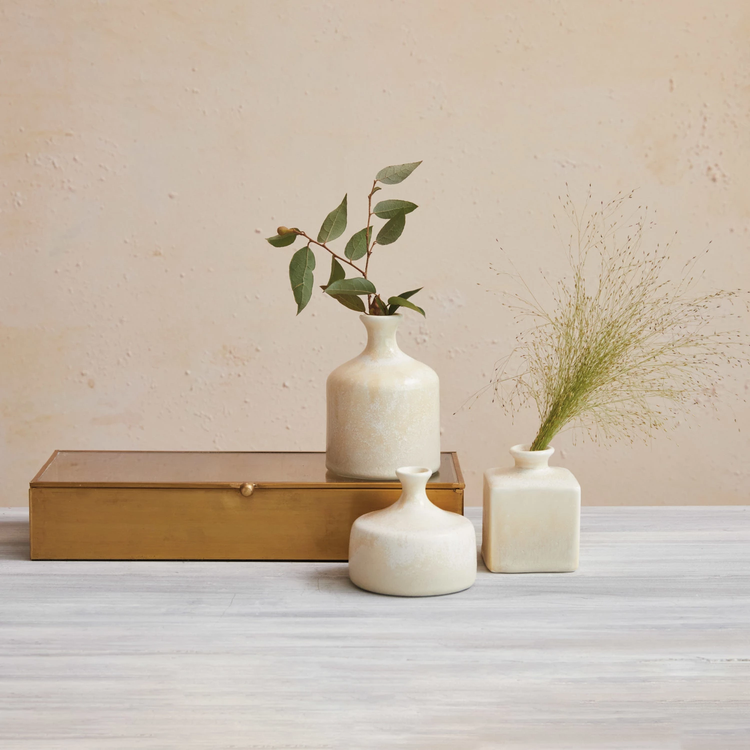 Three cream stoneware vases with reactive glaze in various shapes on a table with a gold box.