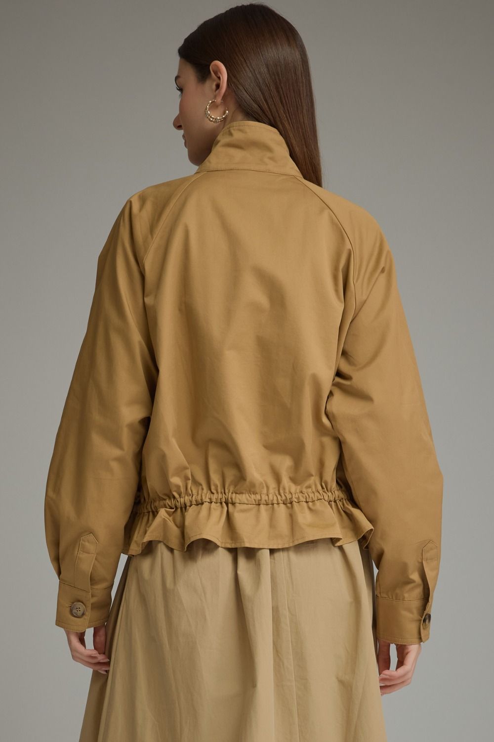 Back view of a woman wearing a tan Andrea solid long sleeve jacket with a ruffled hem.