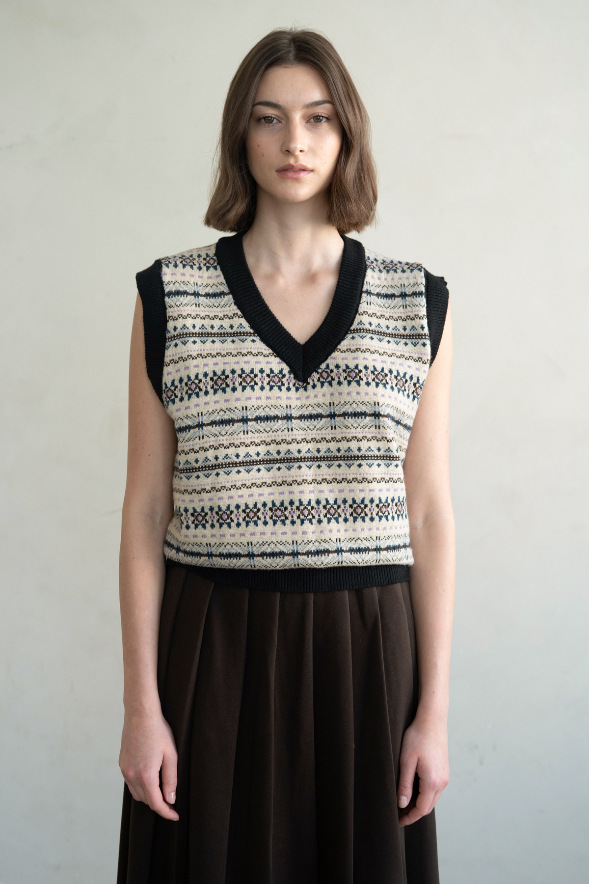 Woman wearing a Via Relaxed Fit Knit Sweater Vest with a fair isle pattern and black V-neck trim.