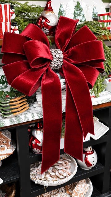 Large red velvet holiday bow with a sparkling rhinestone center knot on a festive display shelf.