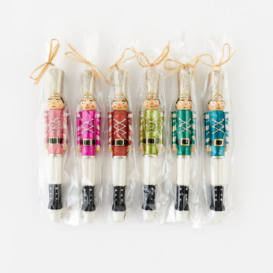 Six colorful nutcracker soldier candles in individual cellophane wraps with raffia bows.