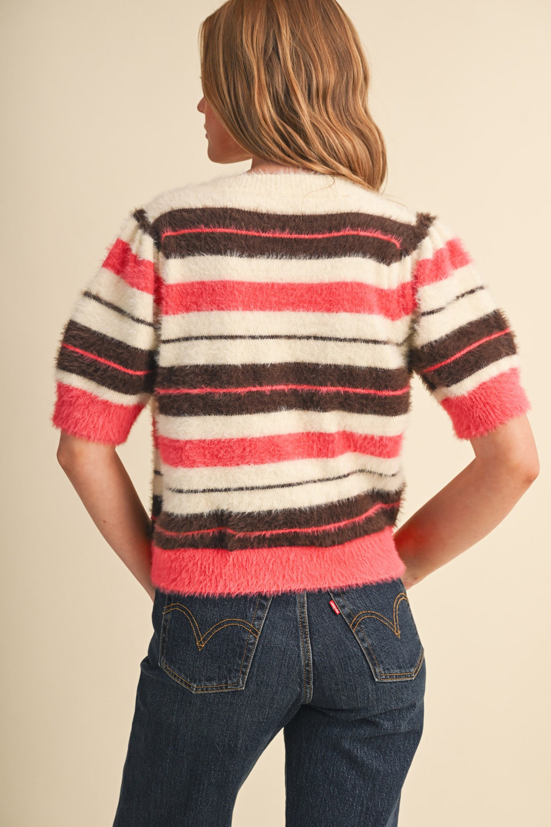 Back view of a woman wearing a fuzzy striped short puff sleeve sweater in pink, brown, and cream.