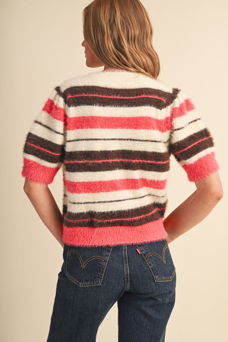 Back view of a woman wearing a fuzzy striped short puff sleeve sweater in pink, brown, and cream.