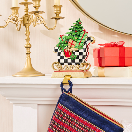 Westminster Sleigh Stocking Holder on a mantel with a checkered sleigh and Christmas tree.