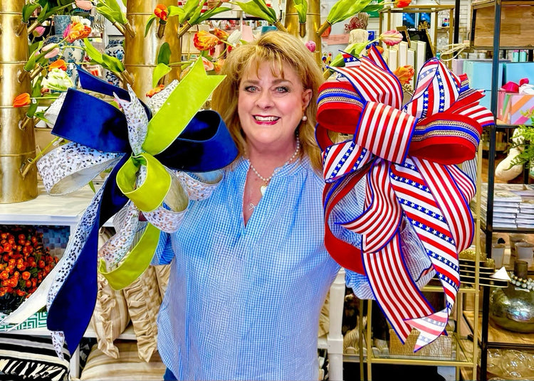 A woman holds two large, handcrafted bows: one blue and lime green, and one patriotic red and white.