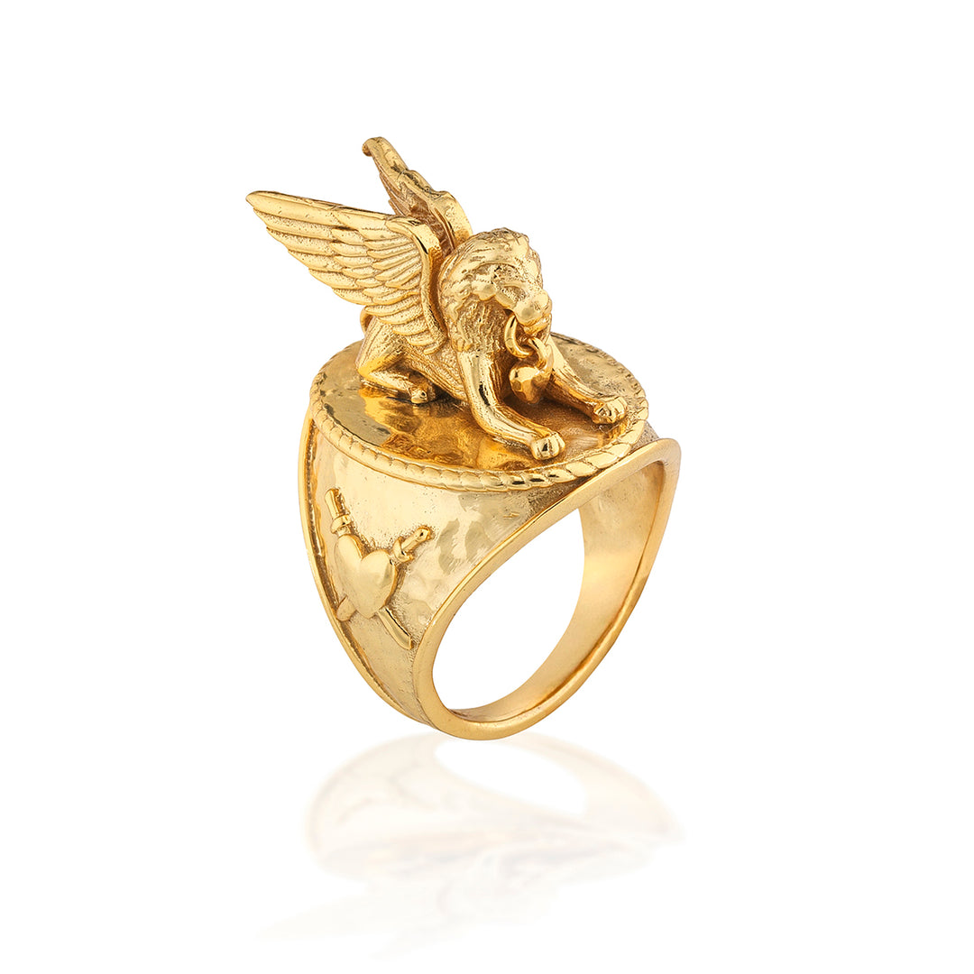 Gold signet-style ring featuring a sculpted winged lion on a textured band with a heart emblem.