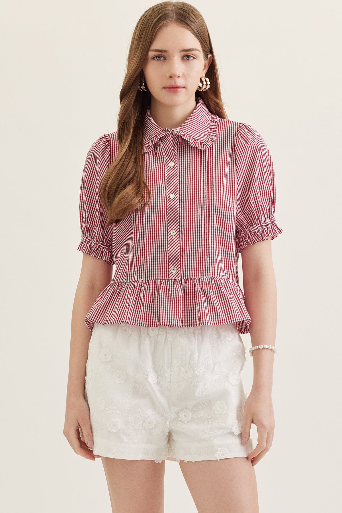 Woman wearing the Katie Collared Blouse in red gingham with puff sleeves and a ruffled hem.