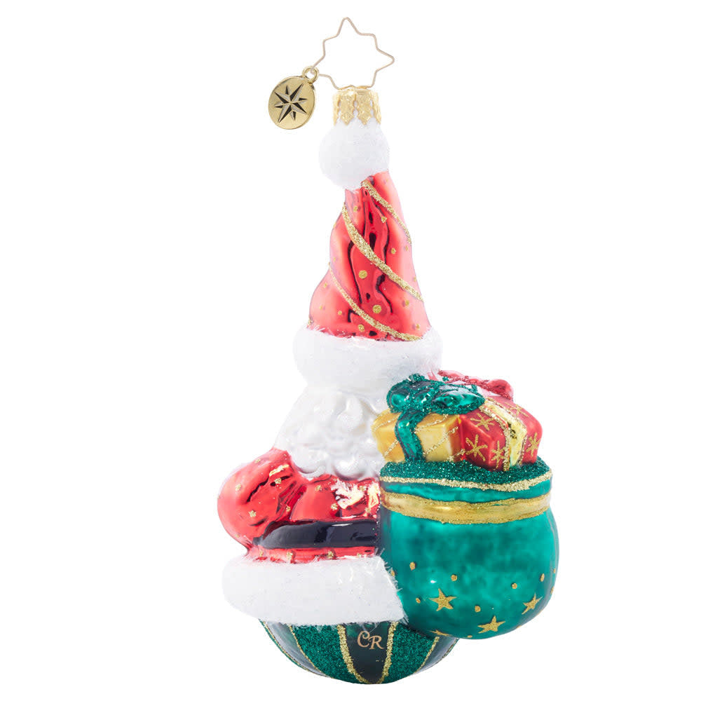 Glass Santa ornament carrying a green sack filled with colorful wrapped gifts.