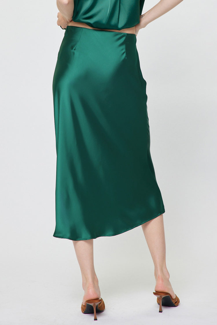 Back view of a woman wearing a green satin midi skirt with an elastic waist and flared bias cut.