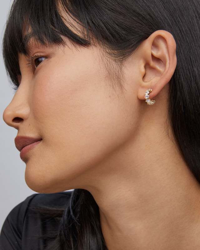 A woman wearing a Cailin Crystal Huggie Earring, a small gold-tone hoop set with clear crystals.