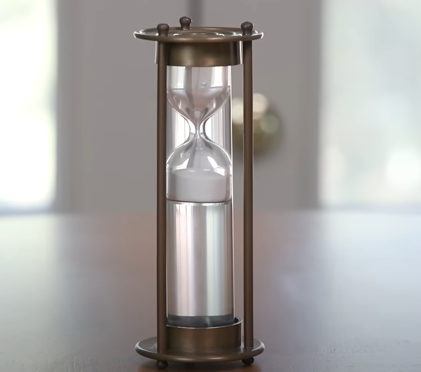 Antique brass sand timer with patina finish featuring a classic hourglass silhouette.