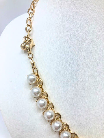Close-up of a gold tone chain necklace featuring a row of round white faux pearls.
