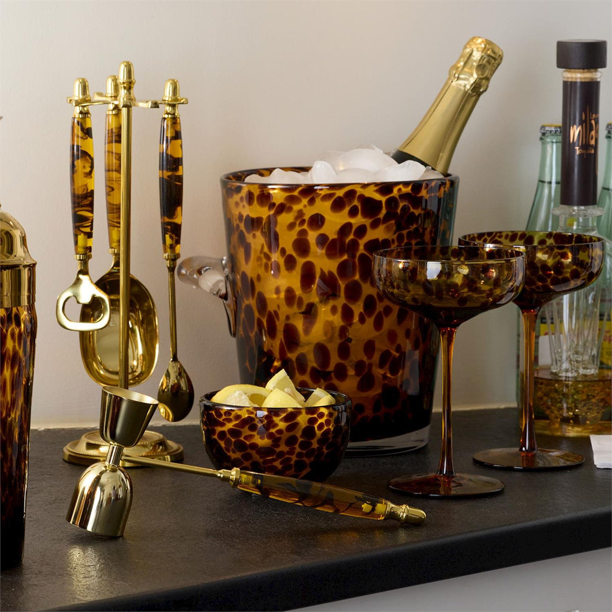 Tortoise print glass ice bucket filled with ice and a champagne bottle on a bar with barware.