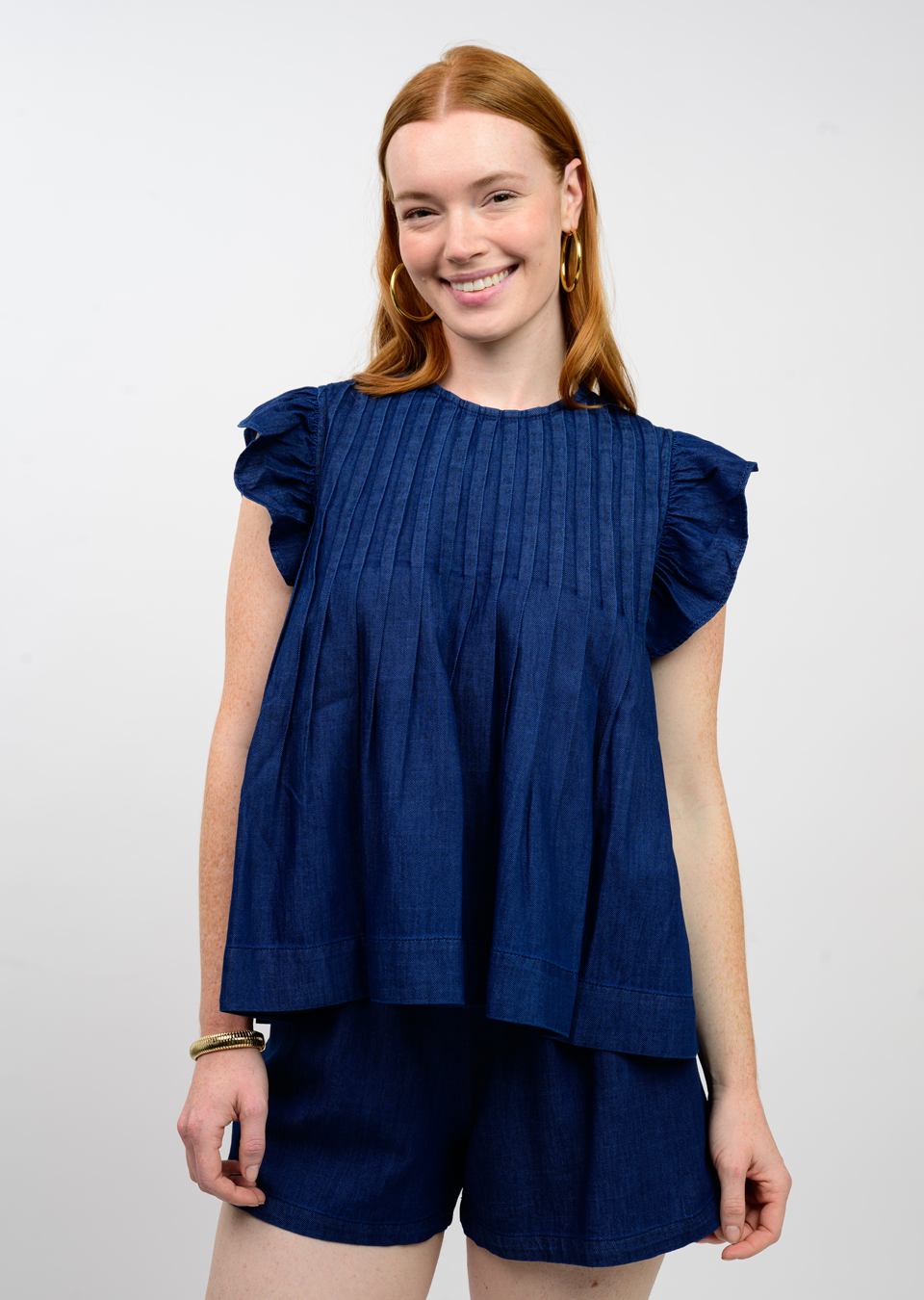 A woman wearing the Carmel Tucked Denim Top in dark blue with ruffled sleeves and pleated details.