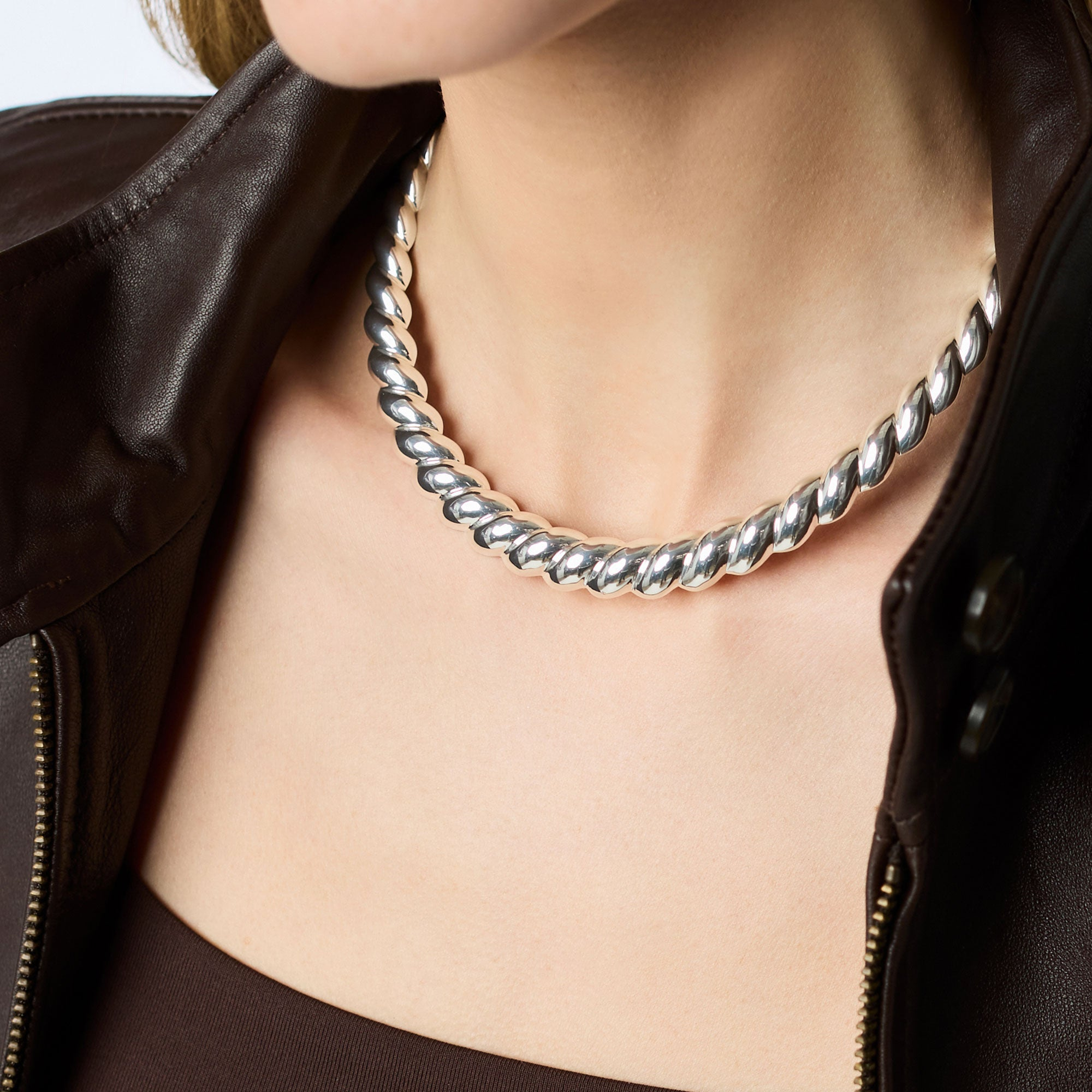 A person wearing the Ravello silver collar necklace with a twisted rope design and a brown jacket.